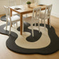 Dining area with a wooden table and white chairs on a black and white patterned rug.