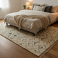 Bedroom with a bed, pillows, and a patterned rug on a wooden floor.