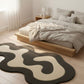 Modern bedroom with a wavy patterned rug on a wooden floor.