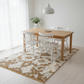 Dining room with wooden table and white chairs on a patterned rug.