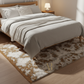 Bedroom with a bed covered in beige bedding and a decorative rug on the floor.
