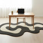Wooden desk with a laptop on a light wood floor with a black and gray patterned rug.