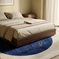 Bedroom with a wooden bed frame, beige bedding, and a blue rug with a logo.