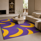 A purple area rug with a bold yellow banana pattern, styled in a modern living room next to a beige sectional sofa and a round stone coffee table.