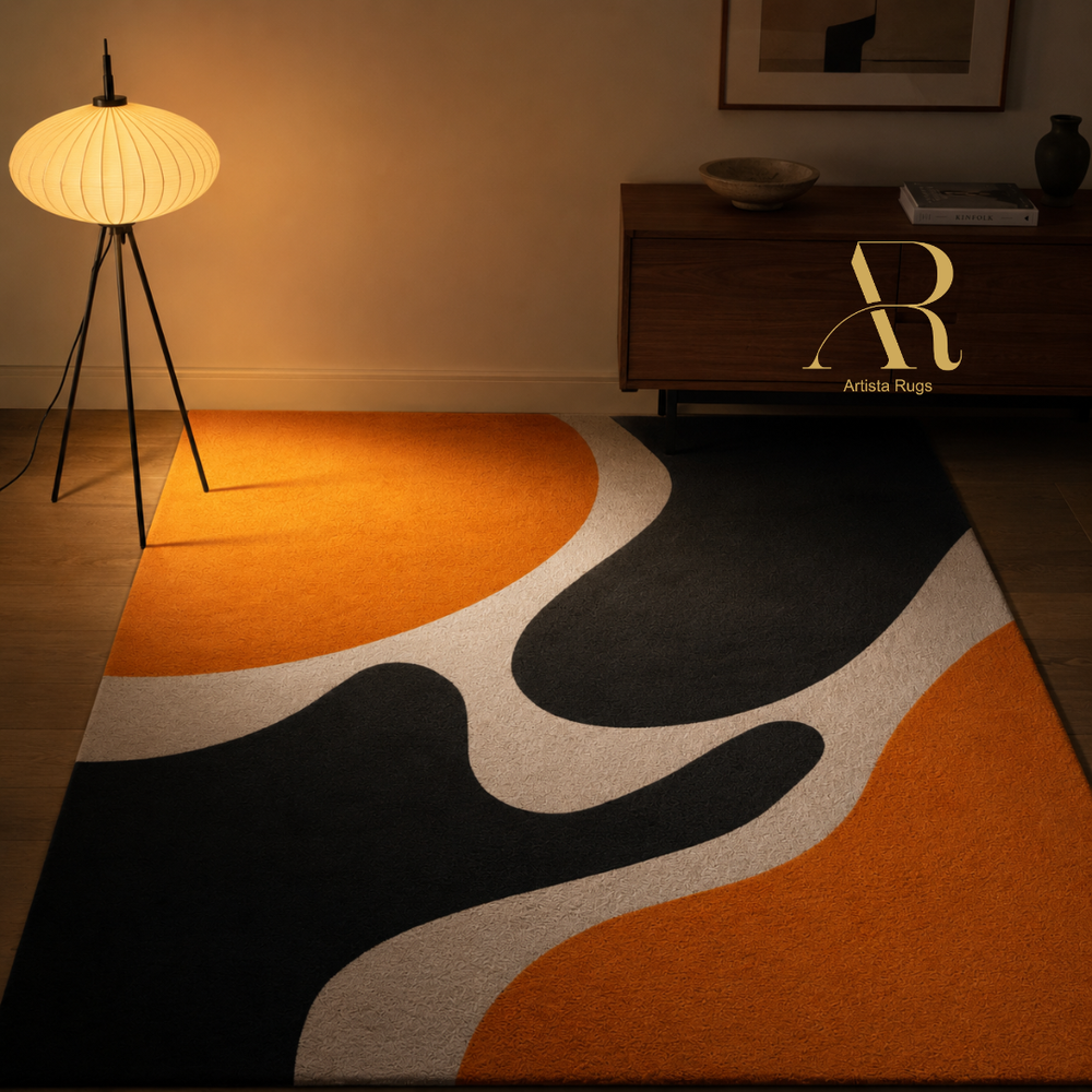 A modern abstract area rug with flowing organic shapes in orange, black, off-white, and gray, styled in a warm, dimly lit room next to a floor lamp and a wooden sideboard.