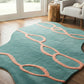 Teal rug with pink patterns on a wooden floor in a room with a chair and side table.