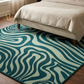 Teal and white patterned rug in front of a bed with beige bedding.