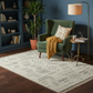 Green armchair with a yellow blanket on a patterned rug in a living room setting.