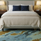 Bedroom with a bed featuring beige bedding and blue pillows, two nightstands with lamps, and a patterned rug.
