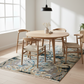 Dining area with wooden table and chairs on a patterned rug in a bright room.