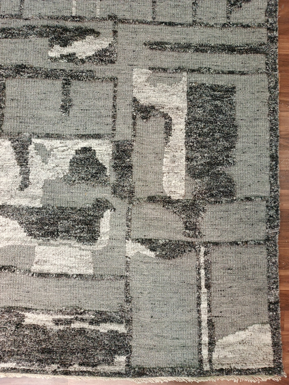 Geometric patterned rug with a mix of gray, black, and white colors on a wooden floor.