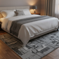 Neatly made bed with white bedding and gray blanket on a patterned rug in a bedroom.