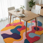 Dining table with chairs on a colorful abstract rug in a bright room.