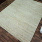 Beige textured rug on a wooden floor with a roll of wallpaper in the corner.