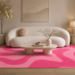 A modern living room scene featuring a bold hot pink and light pink wavy patterned area rug under a curved cream sofa, with a low stone coffee table and neutral decor.