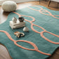 Teal rug with pink patterns on a wooden floor in a living room setting.