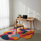 Colorful abstract rug in front of a wooden desk with a laptop.