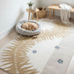 Dog resting on a cushion next to a decorative rug with leaf patterns in a room.