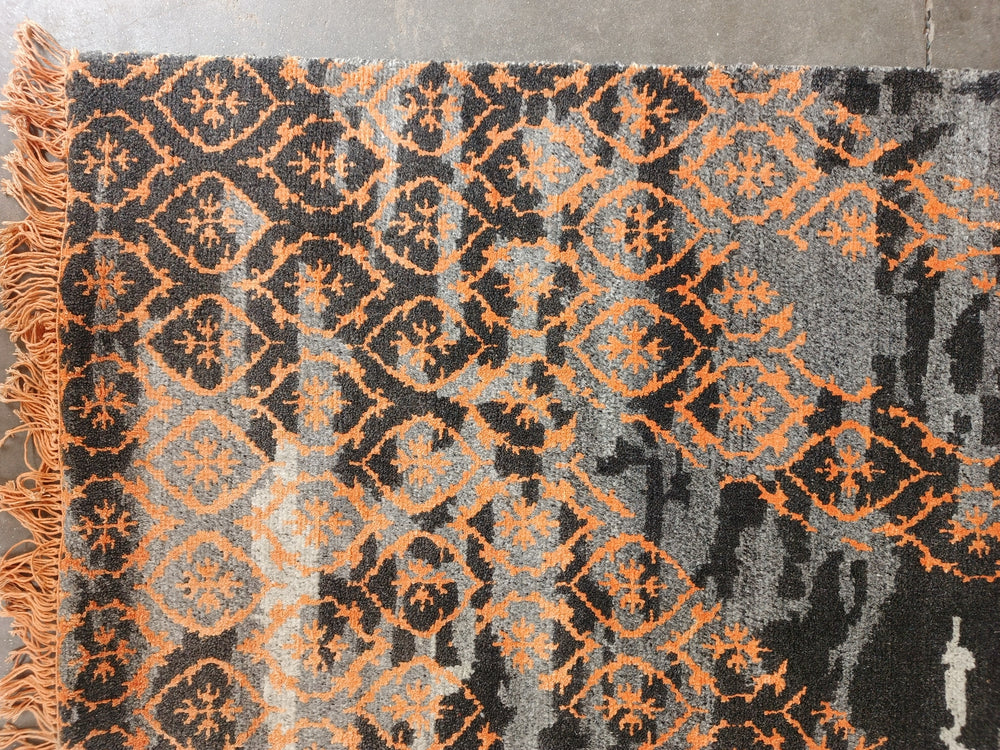 Patterned rug with orange and black design on a gray background