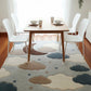 Dining room with a cloud-patterned rug, wooden table, and white chairs.