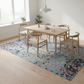 Dining area with wooden table and chairs on a patterned rug in a bright room.