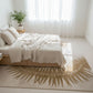 Neatly made bed in a bright room with a palm leaf pattern rug.