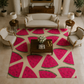 A large area rug with a watermelon slice pattern in bright pink and green on a cream background, styled in a luxurious living room with beige sofas, wooden side tables, and lamps.