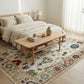 Bedroom with a wooden coffee table on a patterned rug, bed with beige bedding, and nightstand with lamp.