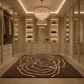 A luxury walk-in closet with cream cabinetry, a large crystal chandelier, and a dark brown area rug featuring a white abstract floral pattern and a small yellow accent.