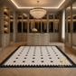 A large rectangular area rug with a black and white geometric pattern is displayed in a luxurious, well-lit walk-in closet. The rug features a black border and a black square motif on a cream background.