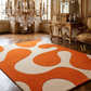 Orange and beige abstract patterned rug in a living room with a beige sofa.