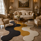 A luxury living room featuring a distinctive wavy area rug in black, mustard yellow, and cream. The room is styled with ornate gold and cream furniture, including a sofa, armchairs, a round wooden coffee table, and matching lamps.