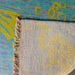 Close-up of a textured rug with a frayed edge and abstract patterns in blue, yellow, and gray.