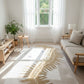 Light-filled living room with a palm leaf patterned rug, wooden furniture, and a large window.