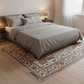 Bedroom with a bed covered in gray bedding on a patterned rug.
