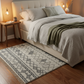 Neatly made bed with green bedding on a wooden floor, featuring a patterned rug.