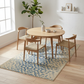 Dining area with wooden table and chairs on a patterned rug in a bright room.