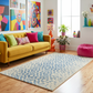 Colorful living room with a yellow sofa, patterned rug, and vibrant artwork.