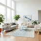 Modern living room with light-colored furniture, plants, and a large window.