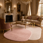 A luxurious living room featuring two round plush area rugs in dusty pink and cream, styled with an ornate gold sofa, matching armchair, marble coffee table, and a grand fireplace.
