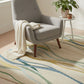 Gray armchair with a white blanket on a colorful rug in a bright room.