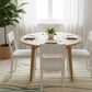 Dining room with a round wooden table and white chairs on a patterned rug.