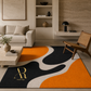 A modern area rug with an abstract wavy pattern in black, orange, and off-white, styled in a contemporary living room setting. The rug features a gold monogram logo for 'Artisa Rugs' in the bottom-left corner.