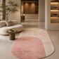 A modern oval area rug in a minimalist living room setting. The rug features a two-tone color-blocked design with a dusty rose pink half and a light beige half, separated by a clean white seam.
