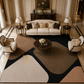 A large modern area rug with abstract organic shapes in beige, brown, black, and blush pink, styled in a luxurious, symmetrical living room with a cream sofa, two armchairs, and a round wooden coffee table.