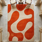 Orange and beige abstract rug on a marble floor with chairs around a table.