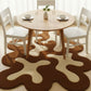 Round wooden dining table with white chairs on a patterned brown and beige rug.