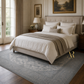 Neatly made bed in a bedroom with a gray rug and framed artwork on the walls.