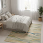 Modern bedroom with a bed and a colorful rug on a light wooden floor.