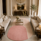 A styled living room with cream sofas, a marble coffee table, and a large oval area rug in blush pink and beige. A smaller round pink rug sits in front.